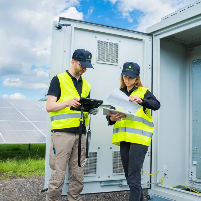 Two greentech technicians check a test report at an open switchgear cabinet