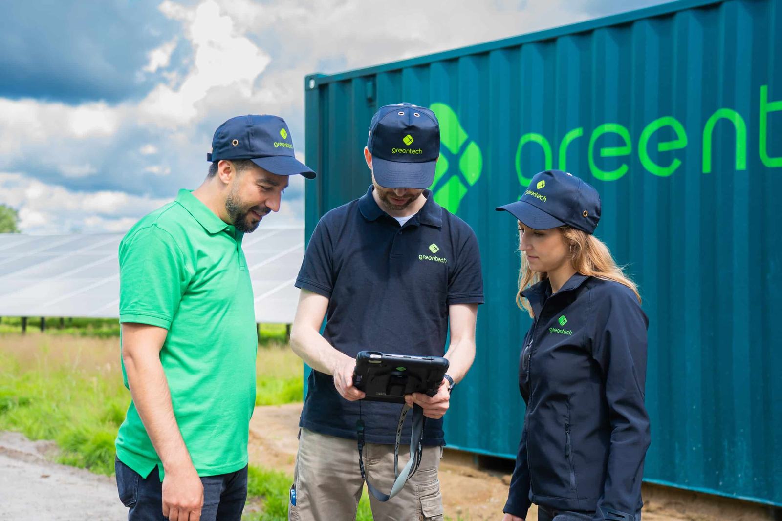 Three greentech colleagues look at a tablet in front of a teal container with the greentech logo