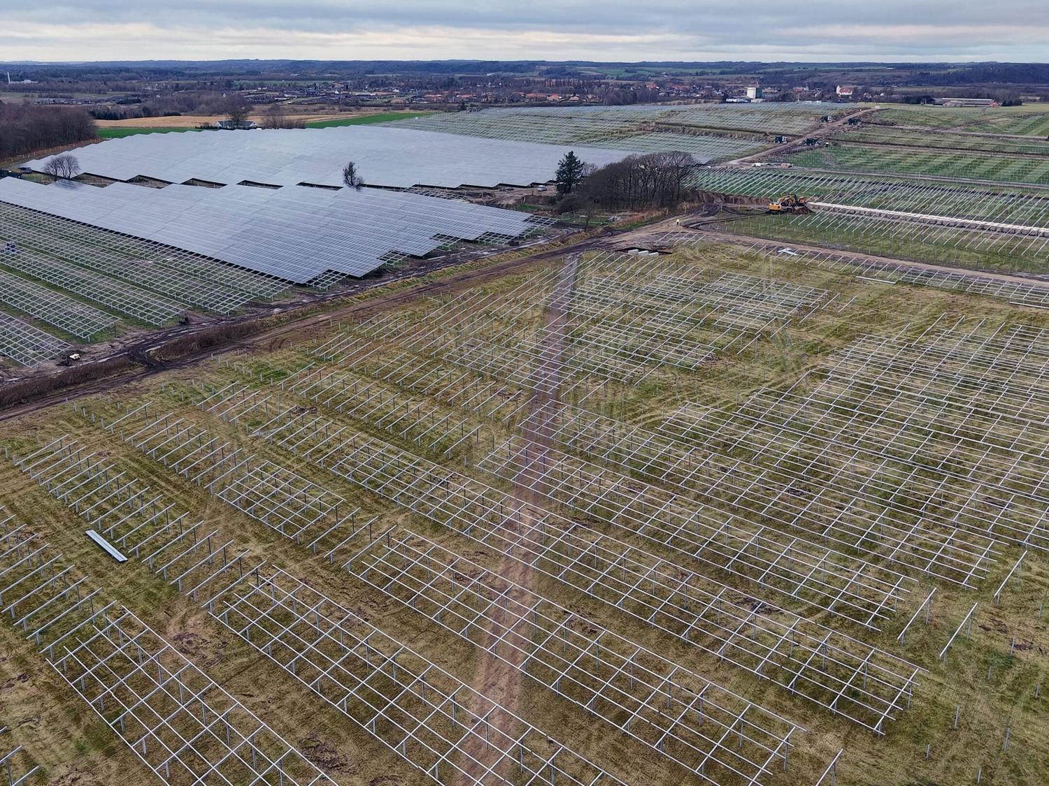 Aerial view of a solar park under construction: finished module rows beside fields of mounting frames.
