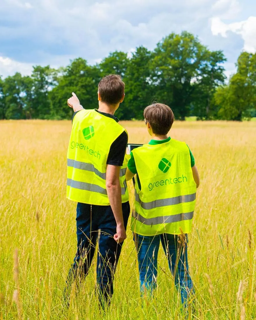 Two greentech developers in high-visibility vests look across a sunlit meadow
