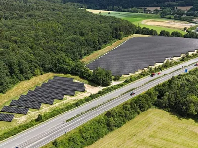 Aerial view of a solar park between a forest and a motorway