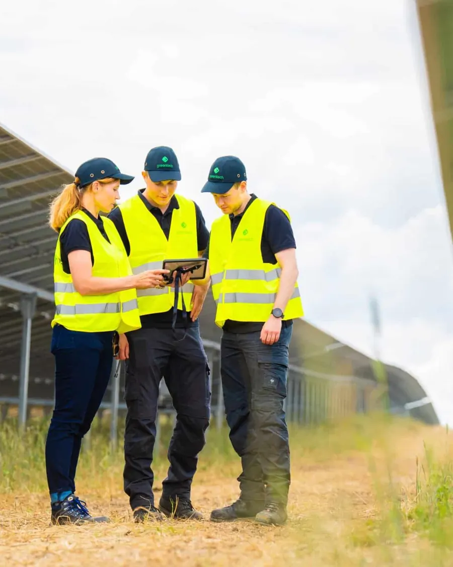 Three greentech technicians check a tablet between rows of modules